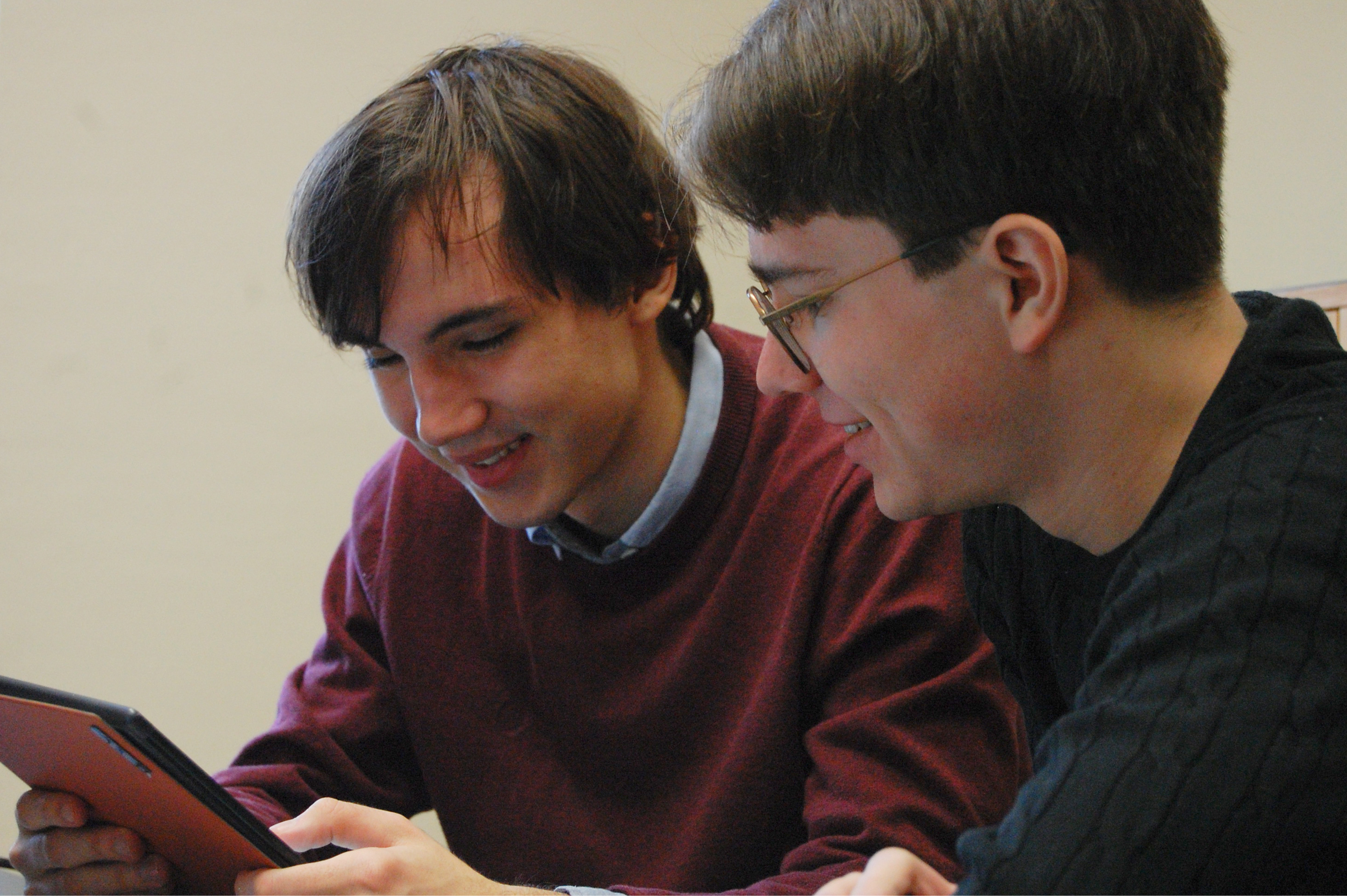 Two young smiling men looking at an e-book reader.