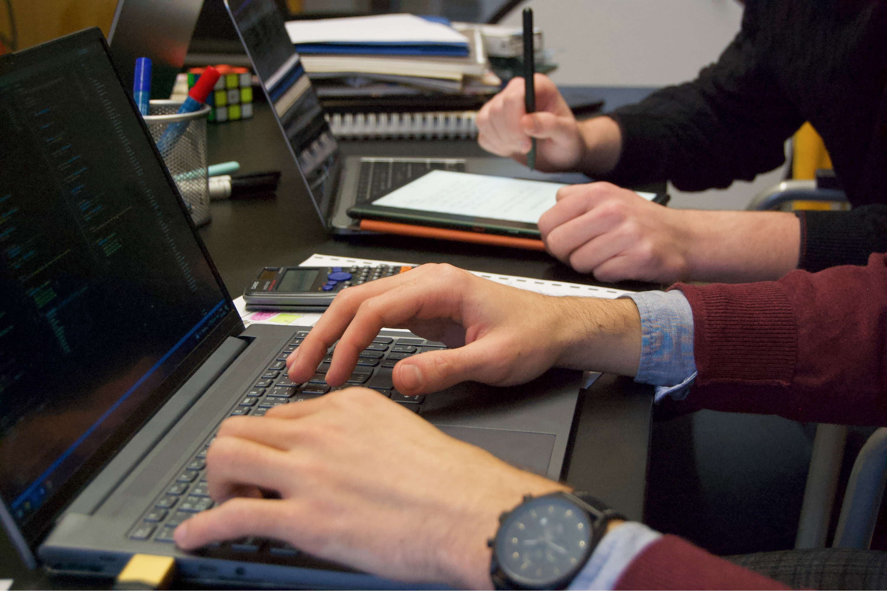 Two men's hands while they work on notebooks.