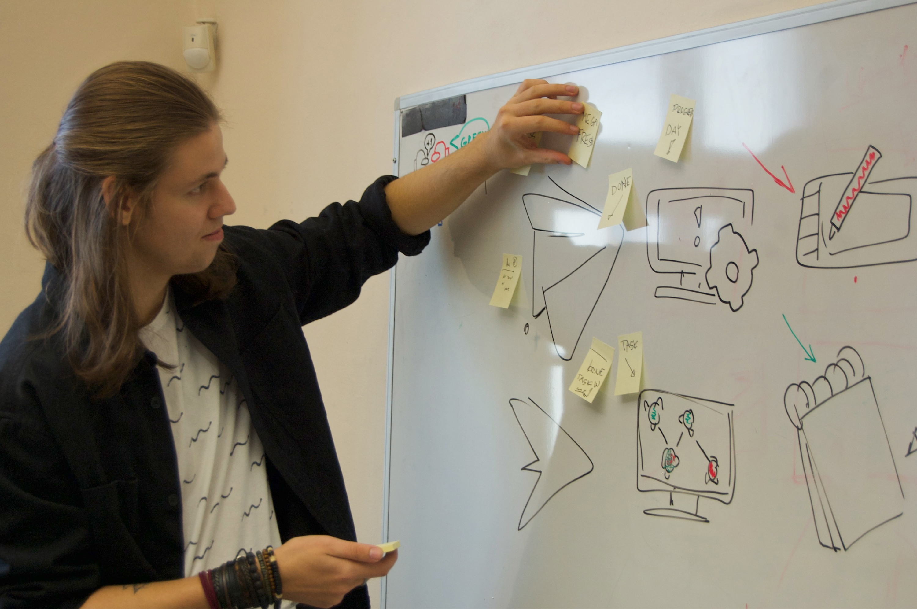 A young man sticking papers to a whiteboard.