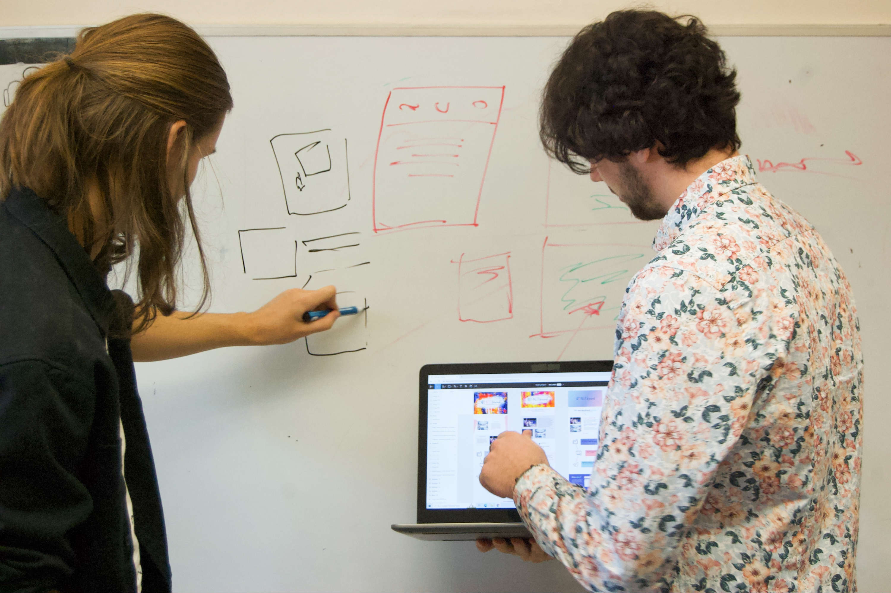 Two men planning a design on a whiteboard and a notebook.
