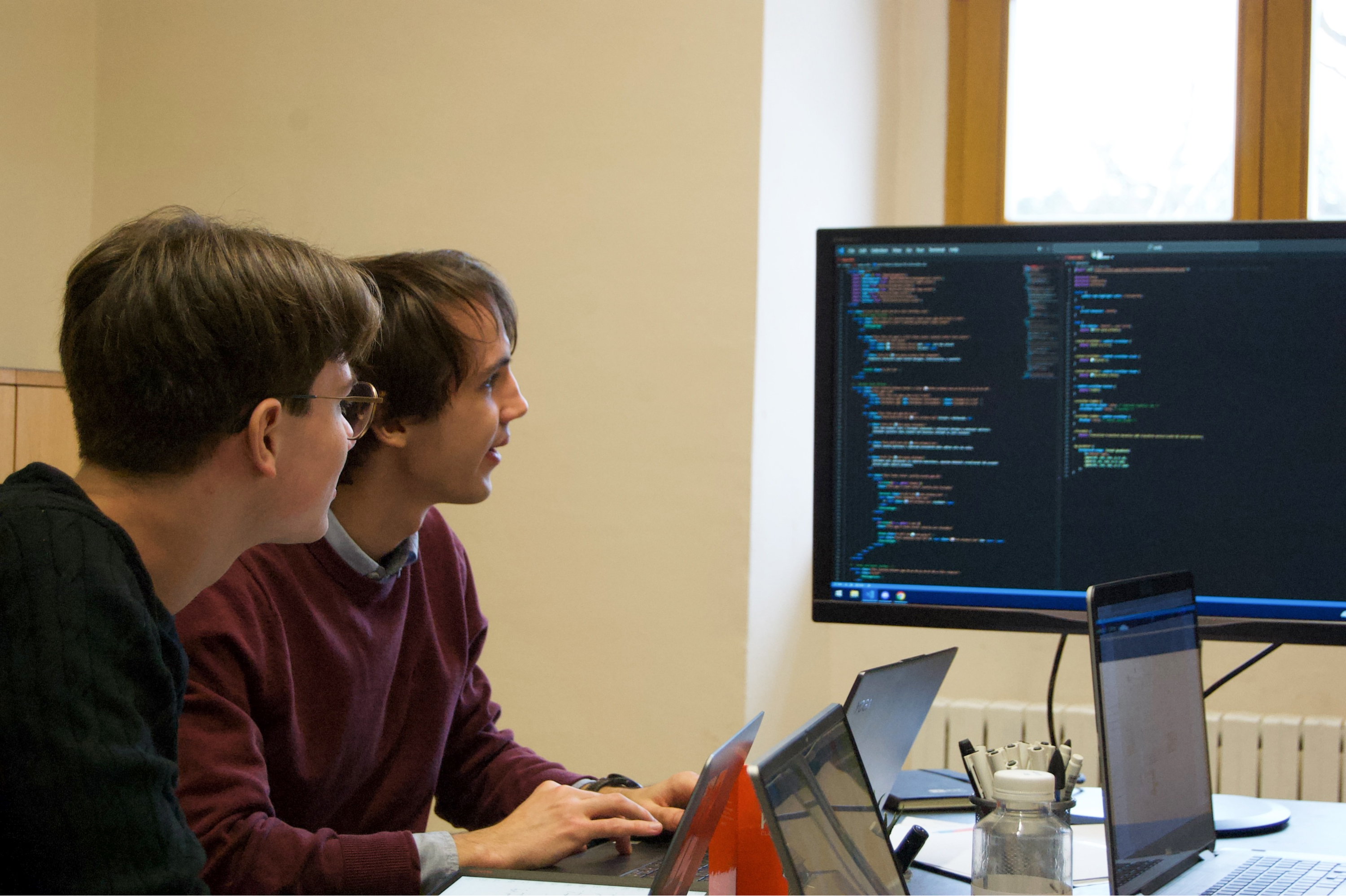 Two developers going through code on a large screen.